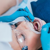 Woman in goggles undergoing dental exam by dentist in blue gloves