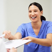 Woman in blue scrubs handing paperwork on clipboard with a pen to patient