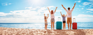Family standing on beach with their suitcases, raising their arms